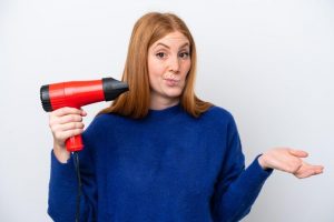 Young redhead woman holding a hairdryer
