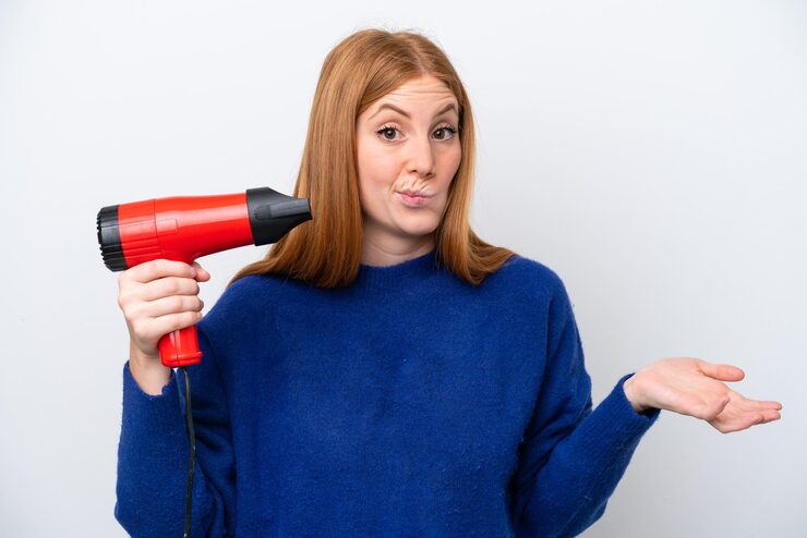Young redhead woman holding a hairdryer